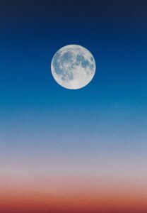 A serene full moon set against a gradient twilight sky, blending hues of blue and orange.